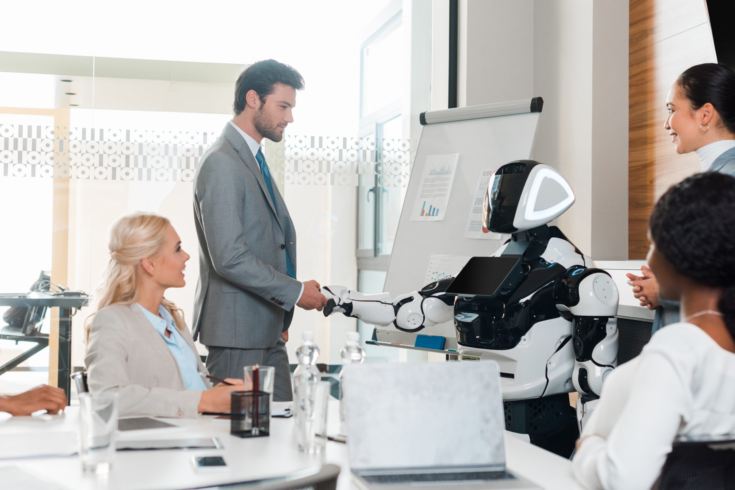 handsome businessman shaking hands with robot near multicultural colleagues sitting in conference